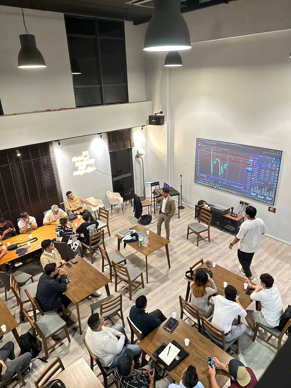 Instructor leading a PounderFX mentorship class beside a trading chart display.